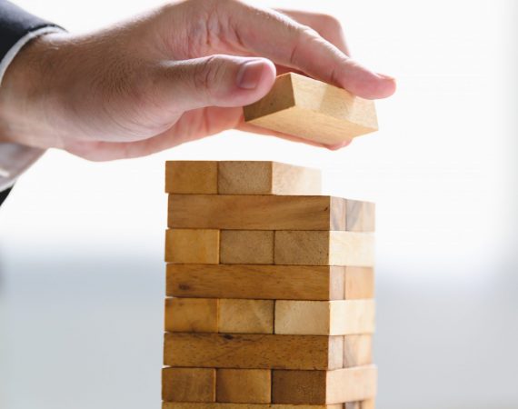Businessman arranging wood block and stacking as tower by hand. Business organization and company growth progress. Success of strategy and money investment concept. Risk management project theme